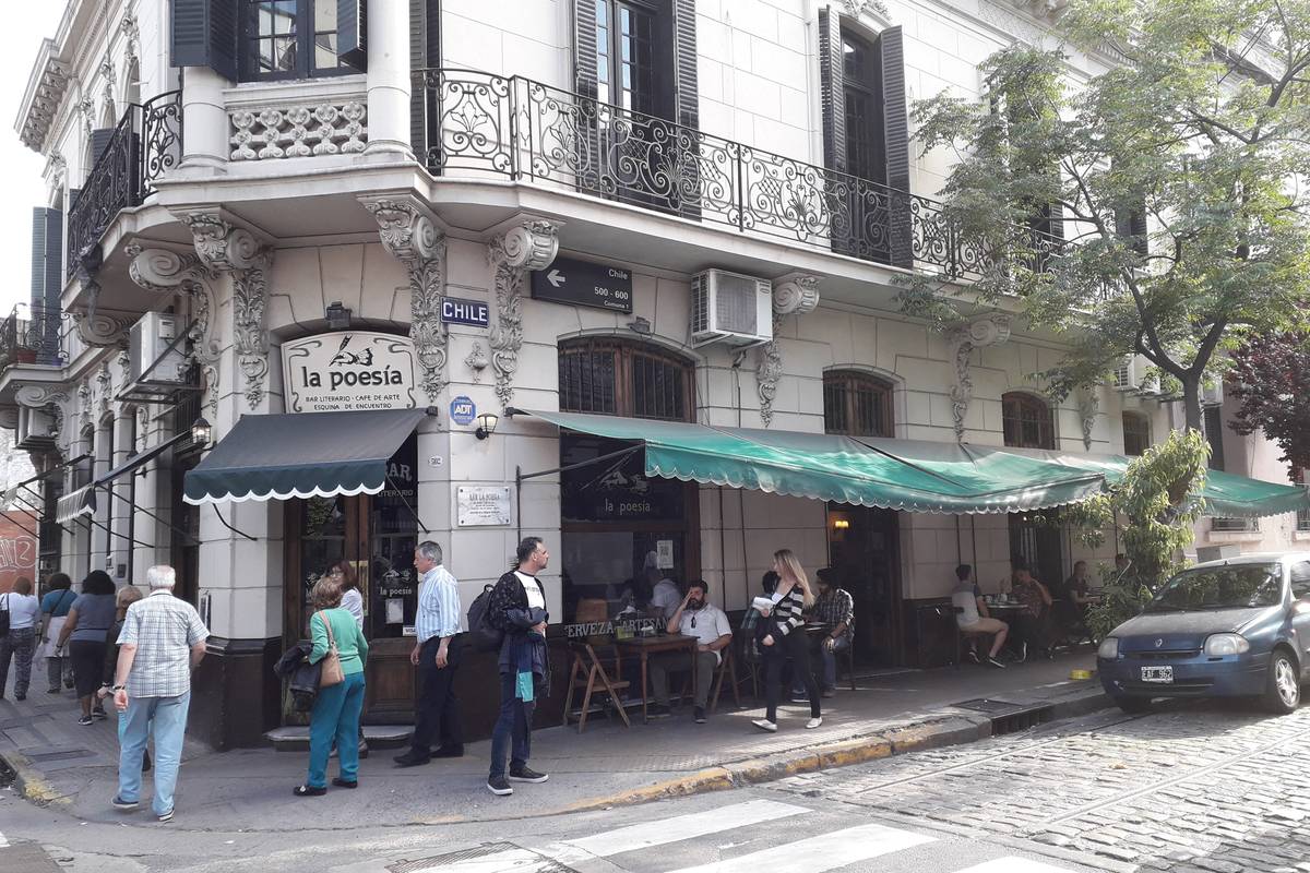 Ett vitt hörnhus med smidesbalkonger och grön markis i San Telmo, där kaféet La Poesía har bord ute vid en gata med kullersten