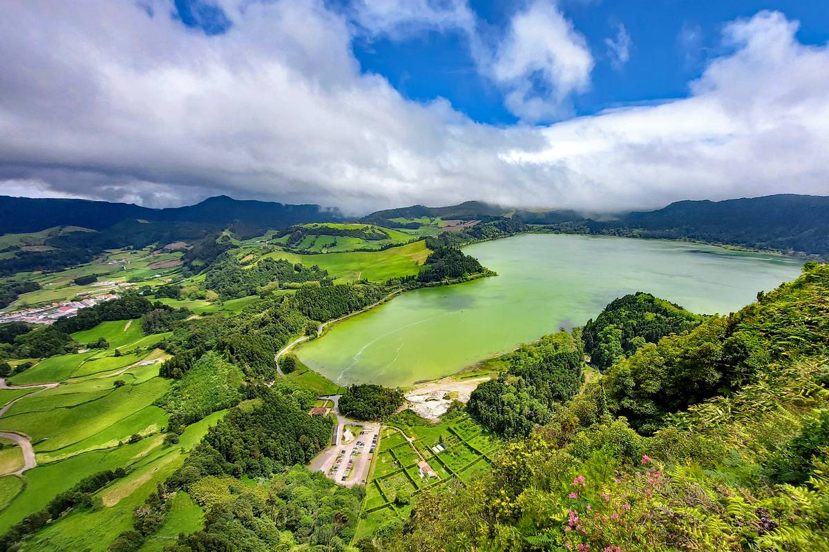 Sjön Lagoa das Furnas i en grön dal på São Miguel sedd uppifrån, med ängar, skog och vita moln över bergen