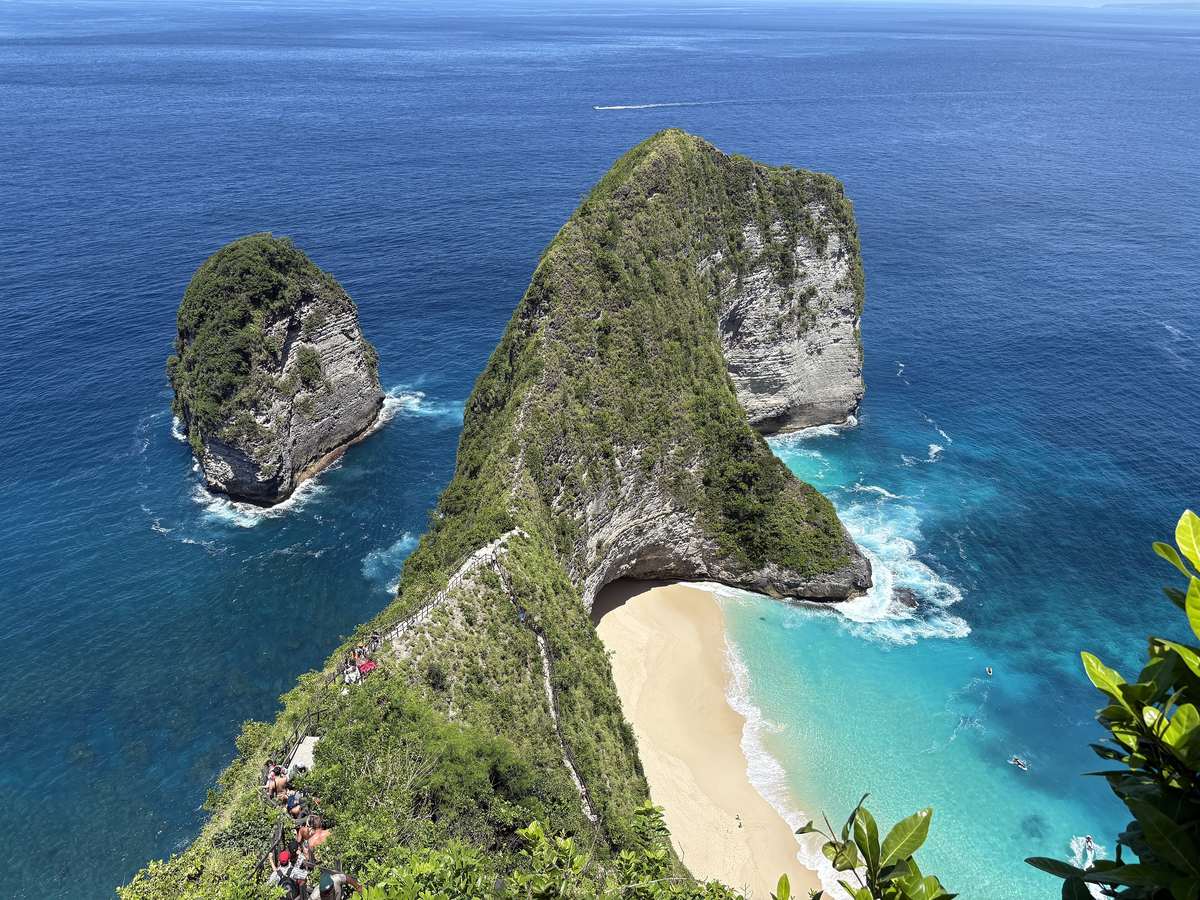 Den grönklädda udden vid Kelingking på Nusa Penida sedd uppifrån, med en ljus sandstrand nedanför och turkost hav runt omkring