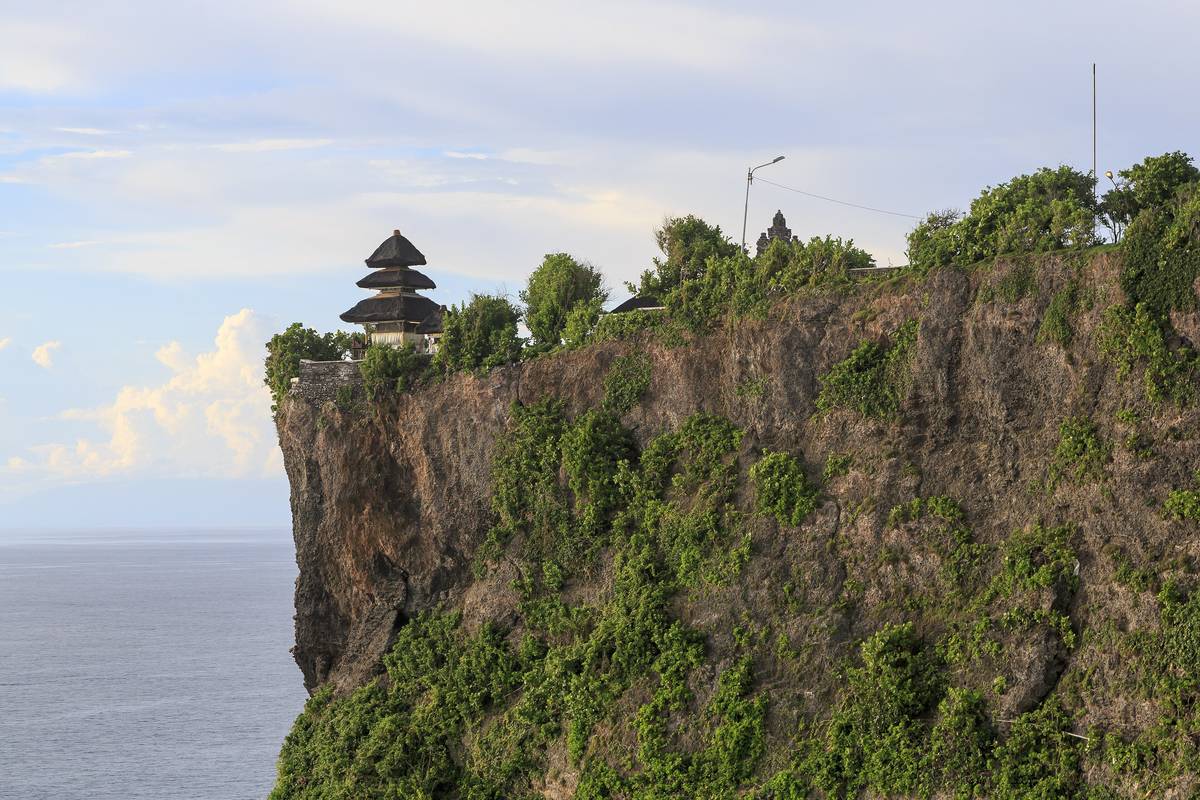 Tempeltornet i Pura Luhur Uluwatu högst upp på en brant, grönklädd kalkstensklippa som stupar rakt ner i havet