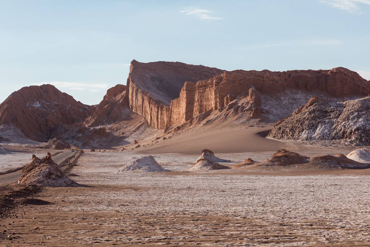 Rödbruna klippväggar och en stor sanddyn i Valle de la Luna med vita saltfläckar och spetsiga klippformationer på den torra marken