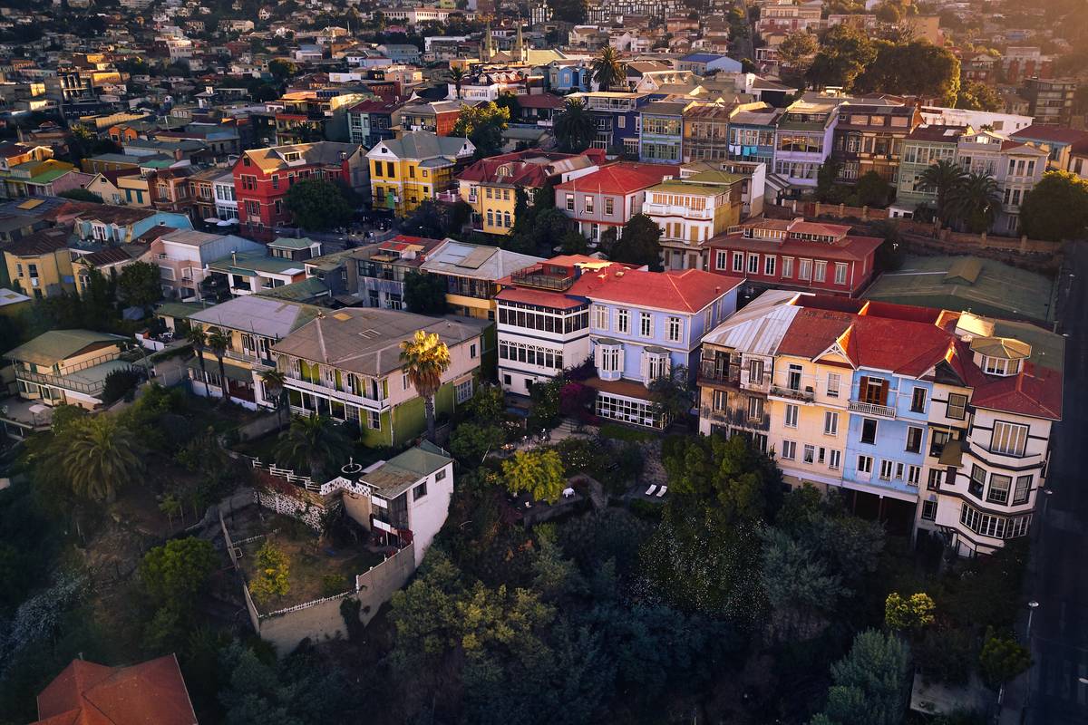 Färgglada hus med röda och gröna tak tätt intill varandra på en kulle i Valparaíso i varmt kvällsljus, sett ovanifrån
