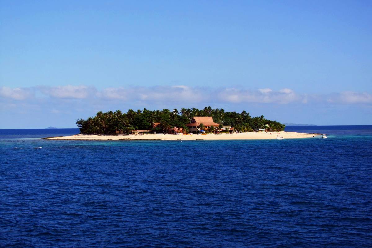 Den lilla platta korallön Beachcomber i Mamanucaöarna med palmer, låga hus och en smal vit strand i djupblått hav