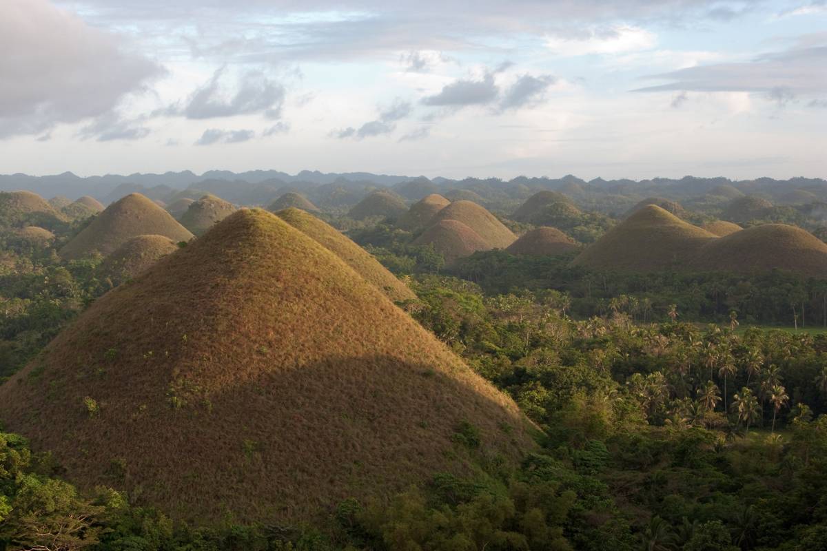 Bruna, kägelformade Chokladkullar på Bohol i kvällsljus, utspridda över ett grönt skogslandskap så långt ögat når