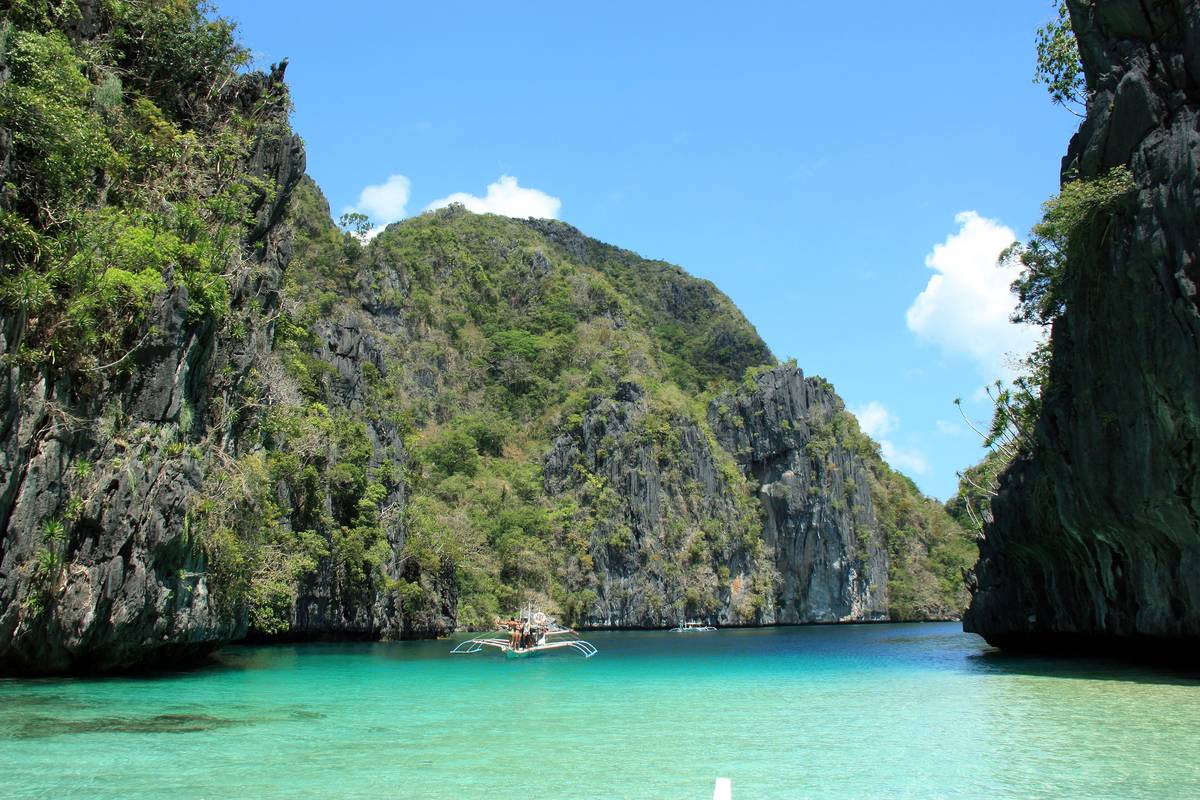 Big Lagoon vid El Nido med turkost, klart vatten omgivet av höga kalkstensklippor täckta av grönska, och en liten båt längst in