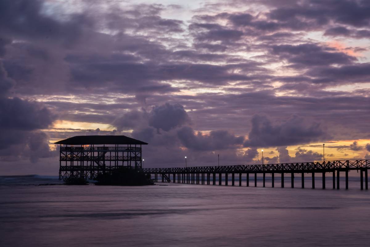 Träbryggan och utsiktstornet vid Cloud 9 på Siargao i siluett mot en lila och rosa himmel i gryningen