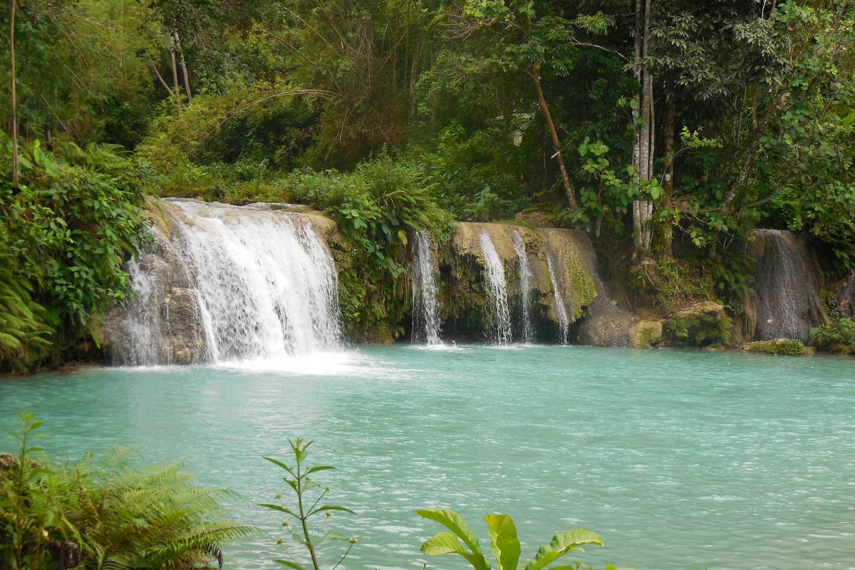 Cambugahay Falls på Siquijor, där vatten forsar ner i flera fall till en turkos pool omgiven av tät grön regnskog