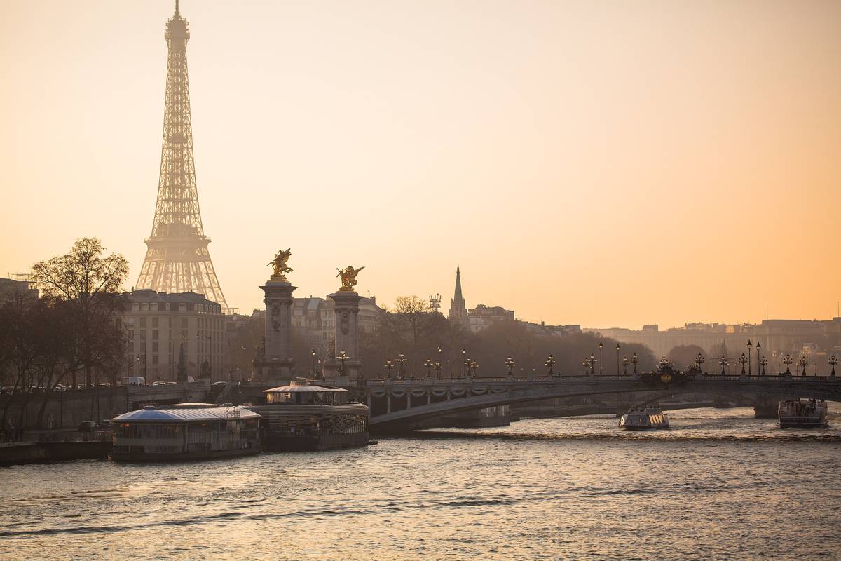 Seinen i Paris i guldfärgat kvällsljus, med Eiffeltornet i siluett, bron Pont Alexandre III med förgyllda statyer och turistbåtar vid kajen