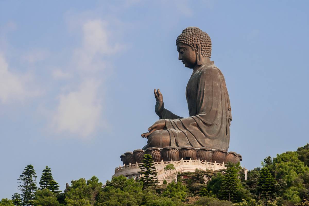 Den stora bronsstatyn Tian Tan Buddha sedd från sidan ovanför gröna träd på Lantau