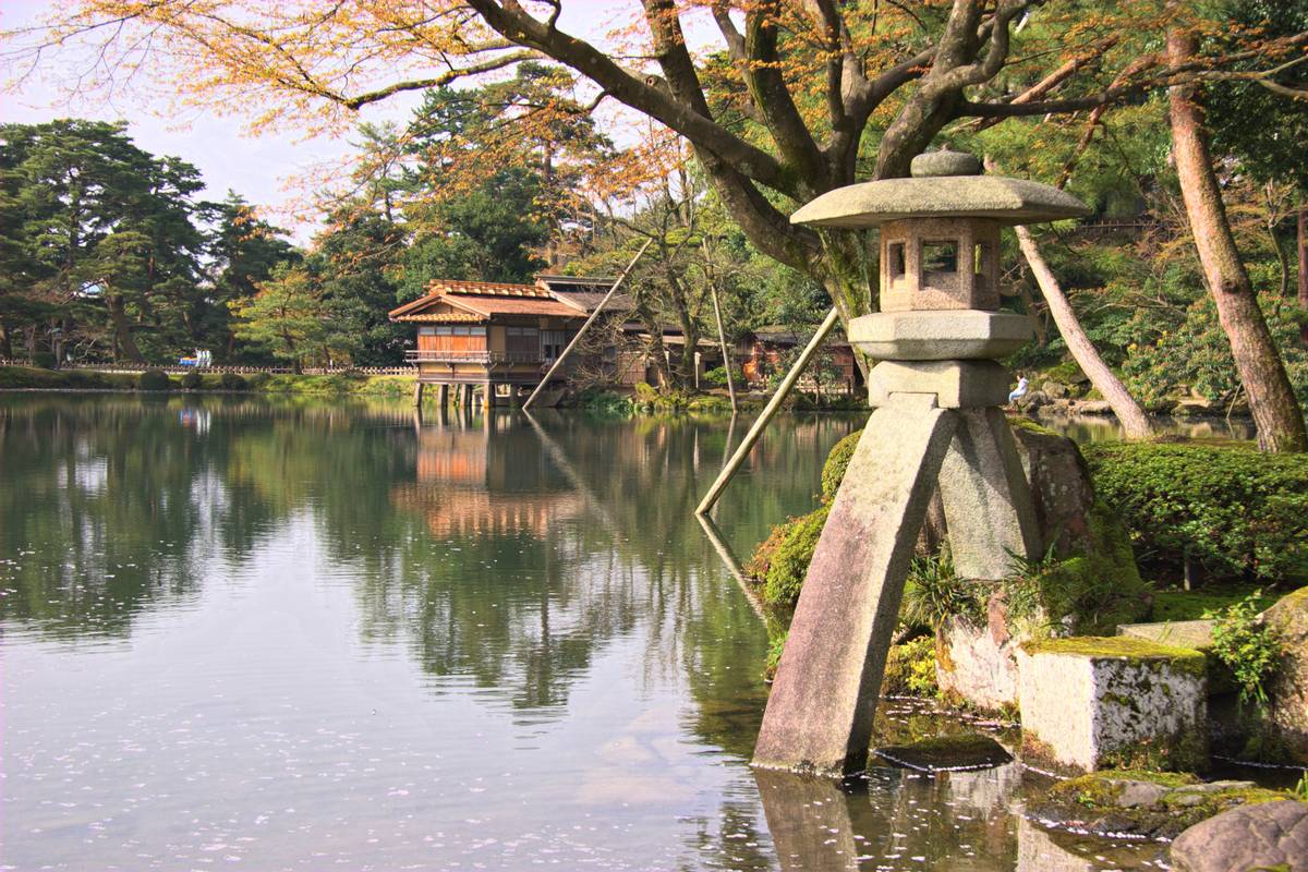Stenlyktan Kotoji med sina två ben står vid kanten av en damm i trädgården Kenroku-en i Kanazawa, omgiven av grönska