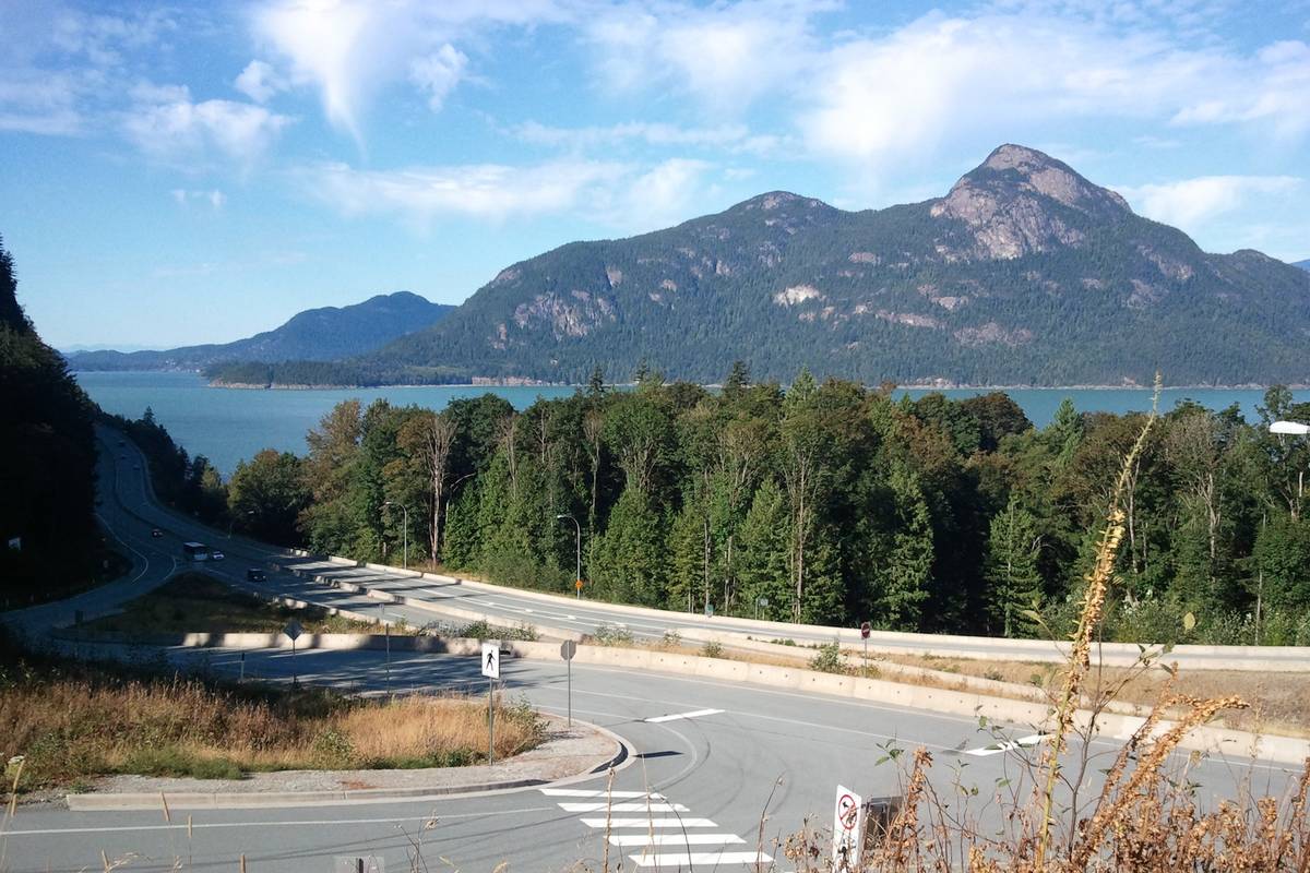 Sea to Sky Highway slingrar sig genom granskogen vid Howe Sound, med fjordens blå vatten och ett skogklätt berg i bakgrunden