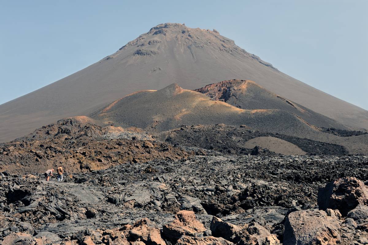 Vulkanen Pico do Fogo på ön Fogo med en mindre, rödbrun sidokon framför och svarta lavafält i förgrunden under blå himmel