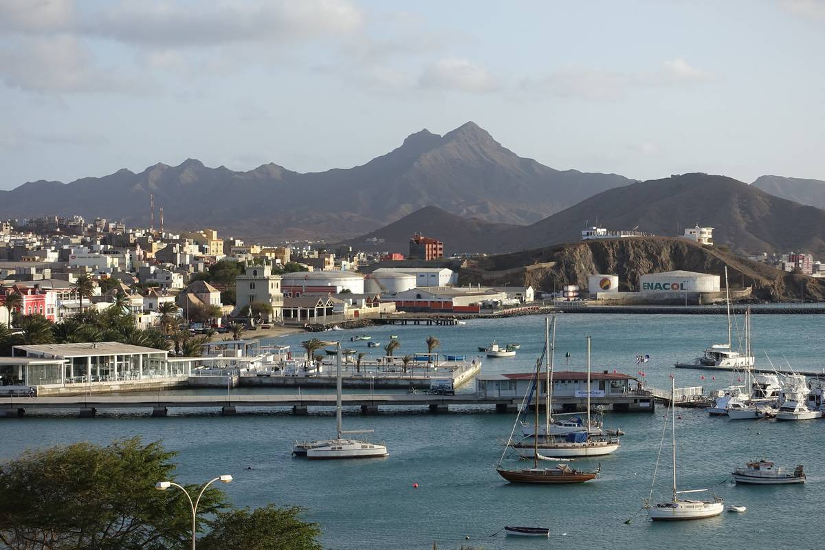 Hamnen i Mindelo på São Vicente med segelbåtar i viken, färgglada hus längs stranden och berget Monte Cara i eftermiddagsljus bakom staden