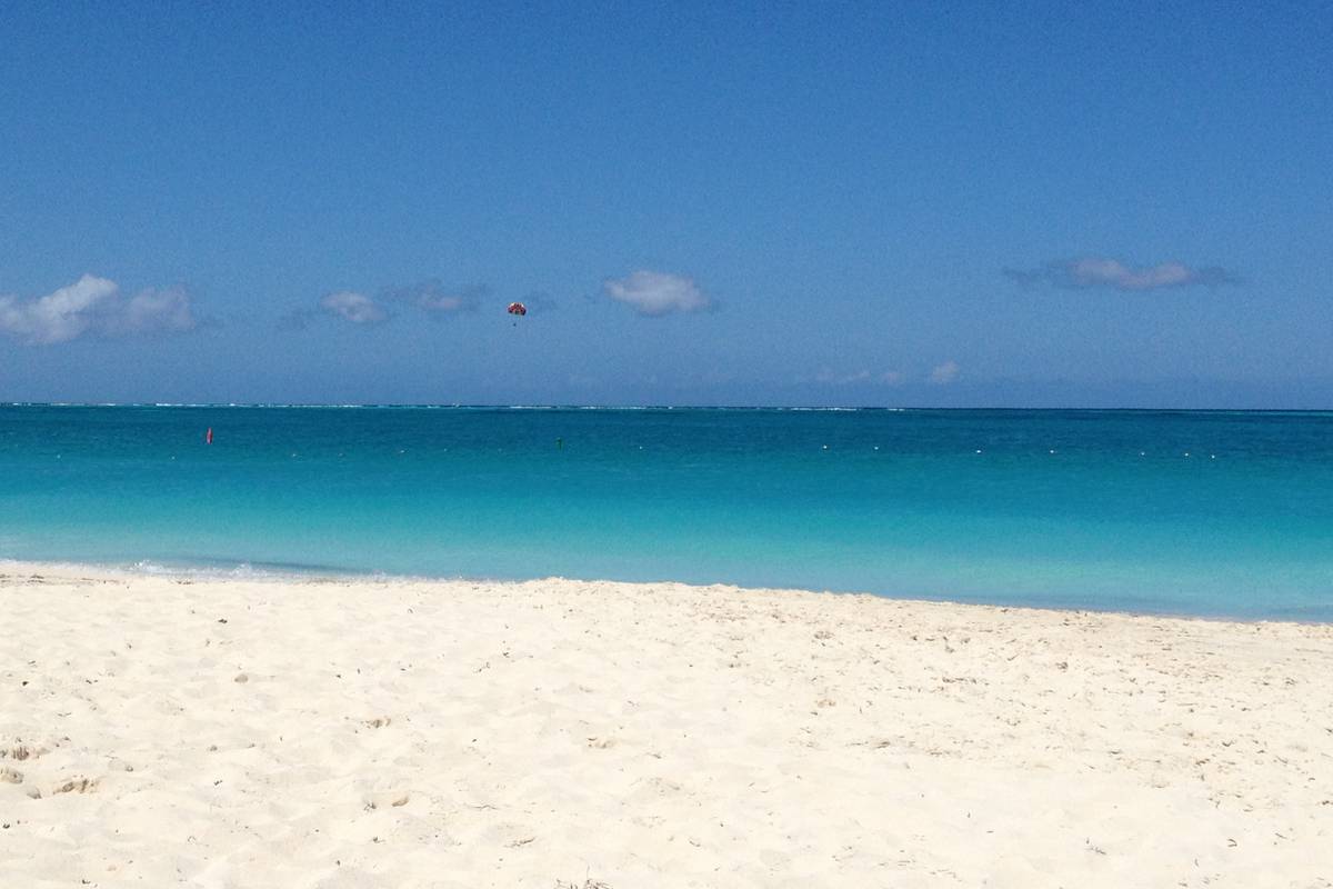 Pudervit sand och klart turkost vatten under blå himmel på Grace Bay
