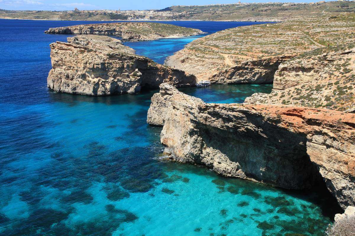 Turkost och klart vatten i Blå lagunen vid Comino mellan ljusa kalkstensklippor, med Cominotto och Gozo i bakgrunden