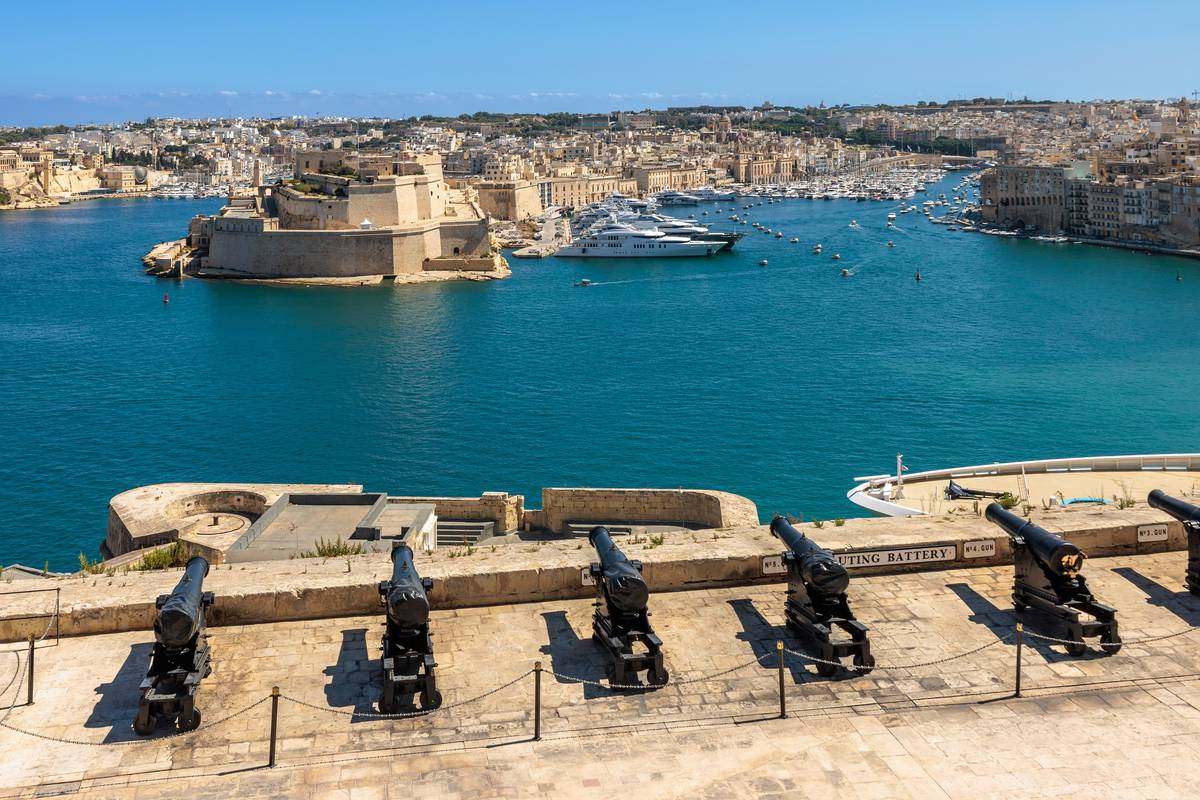 Svarta kanoner på Saluting Battery i Upper Barrakka Gardens med utsikt över det turkosa vattnet i Grand Harbour och Fort St Angelo