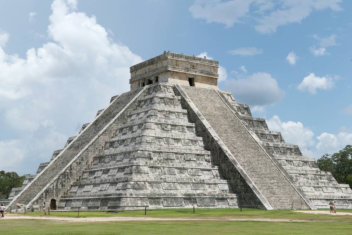 Den fyrsidiga stegpyramiden El Castillo med ett tempel på toppen, på en grön gräsmatta under blå himmel och vita moln i Chichén Itzá
