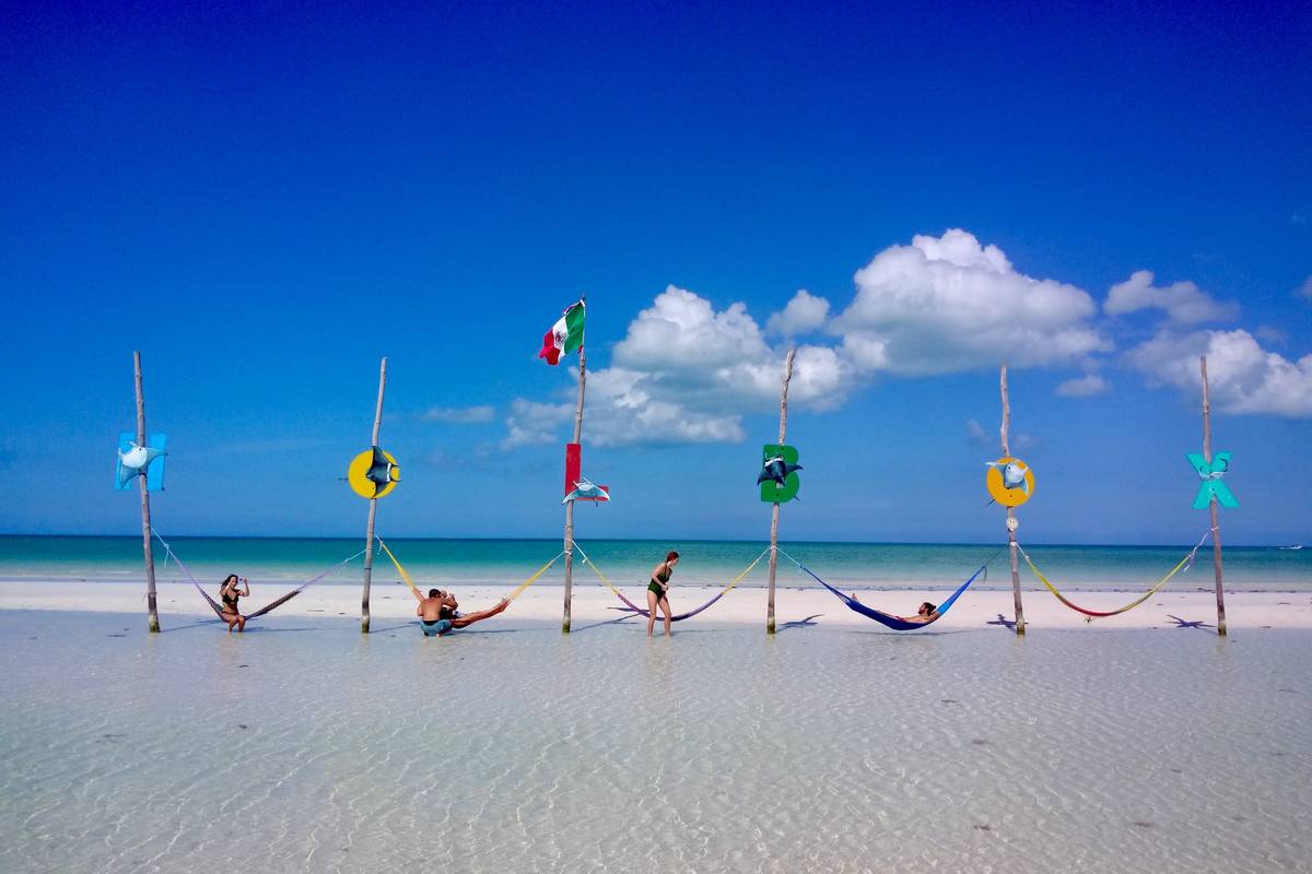 Färgglada hängmattor uppspända mellan pålar i det grunda, klara vattnet utanför den vita stranden på Holbox under blå himmel