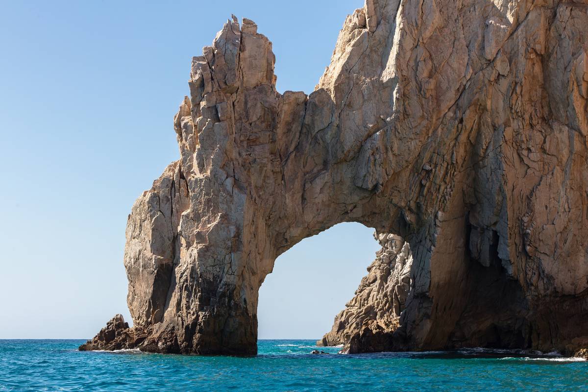 Klippbågen El Arco i ljusbrun granit som reser sig ur turkost hav vid Land's End under klarblå himmel