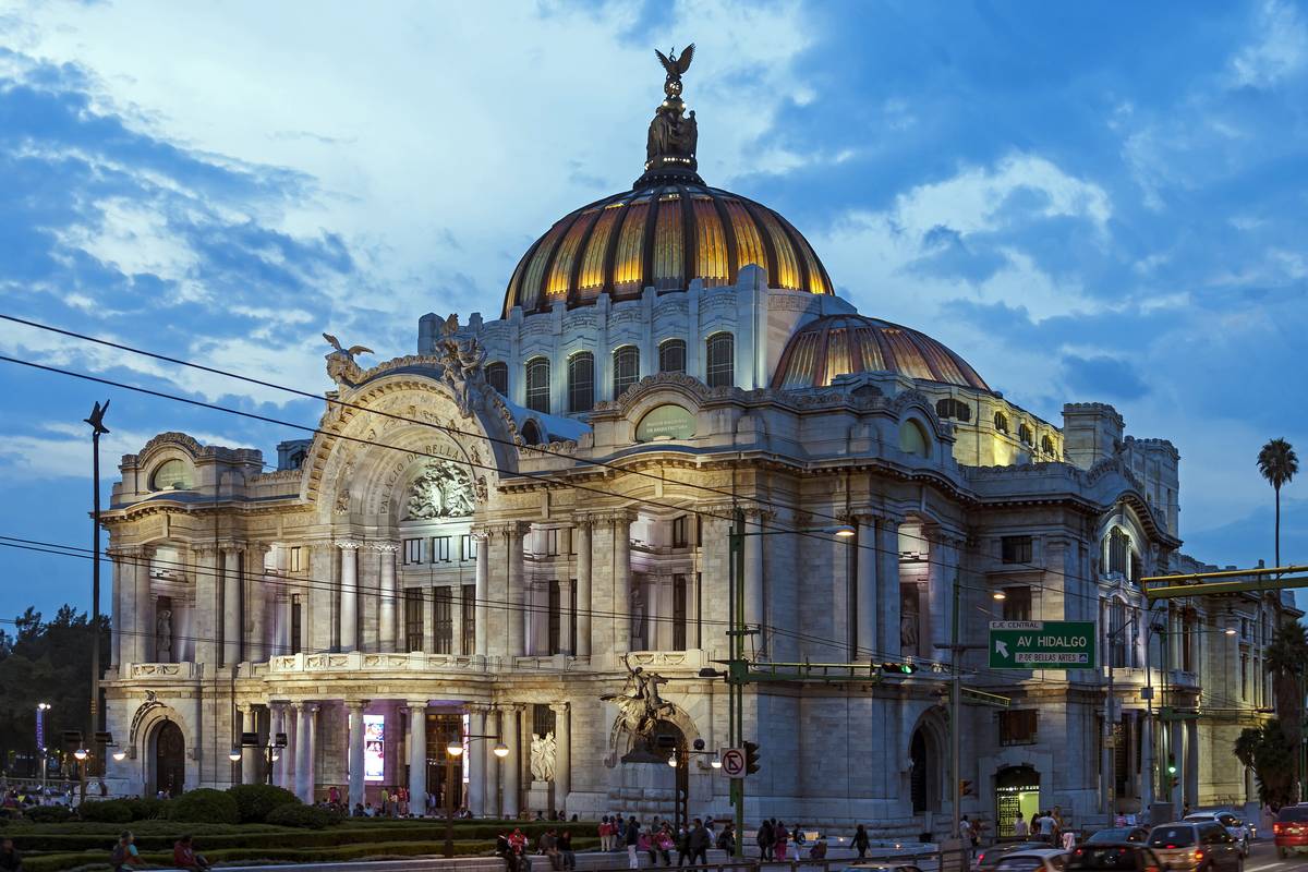 Palacio de Bellas Artes med gyllene kupoler och upplyst vit marmorfasad i skymningen under en blå himmel i Mexico City