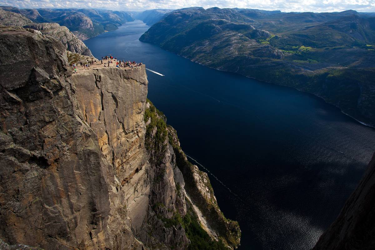 Klippavsatsen Preikestolen med lodräta väggar högt ovanför den mörkblå Lysefjorden, med skogklädda berg på andra sidan fjorden
