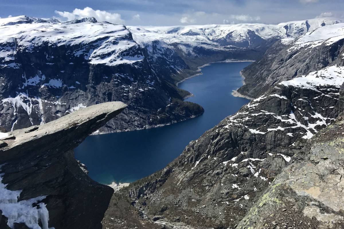 Klipptungan Trolltunga sticker ut horisontellt över en djup dal med sjön Ringedalsvatnet, omgiven av berg med snöfläckar