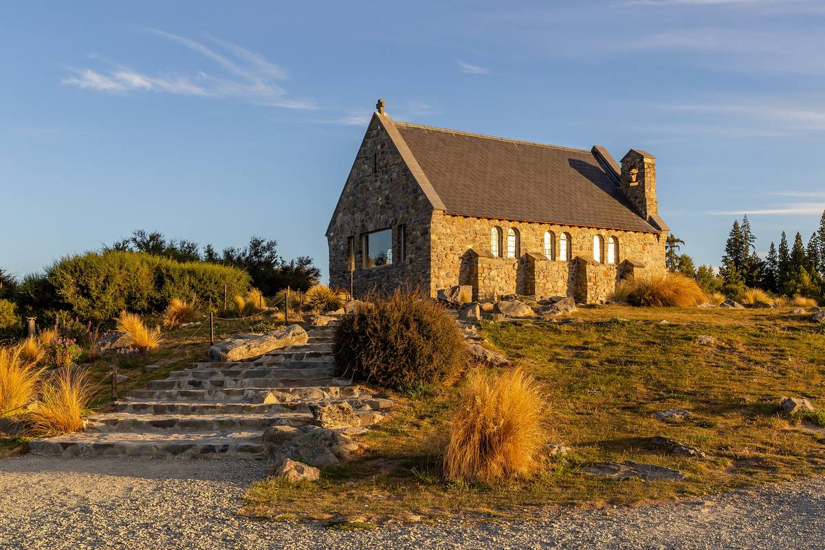 Den lilla stenkyrkan Church of the Good Shepherd vid Lake Tekapo i kvällssol, med stentrappa och gyllene tuvgräs framför