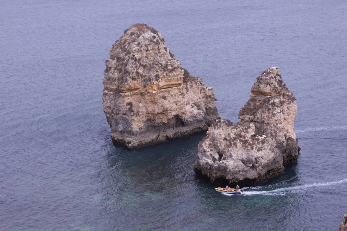 Två höga kalkstensklippor som reser sig ur blått vatten vid Ponta da Piedade nära Lagos i Algarve, med en liten turistbåt nedanför