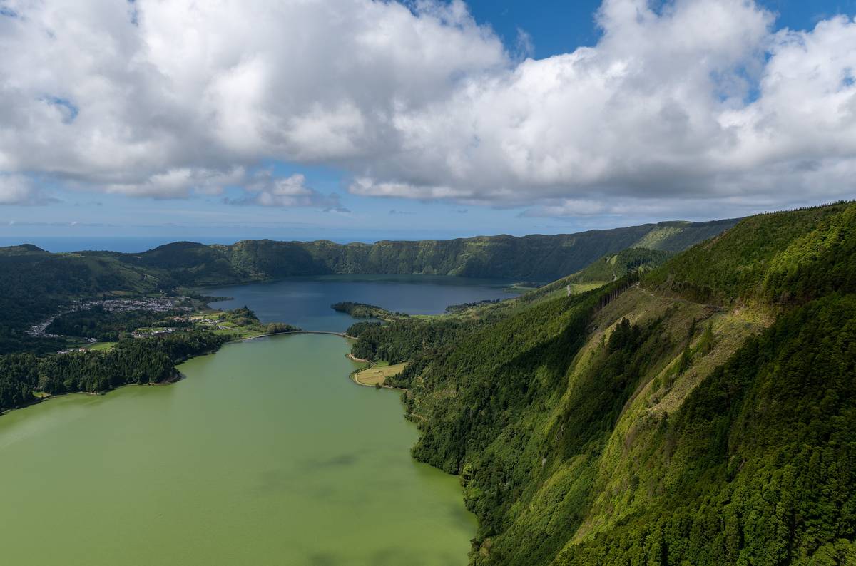 Den gröna och den blå kratersjön vid Sete Cidades på São Miguel, omgivna av gröna kraterväggar och byn vid stranden, under vita moln