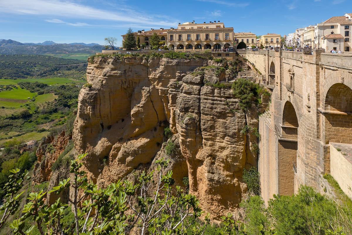 Bron Puente Nuevo i Ronda, byggd av sten över den djupa ravinen El Tajo, med vita hus och en parador på klippkanten och gröna dalar bakom