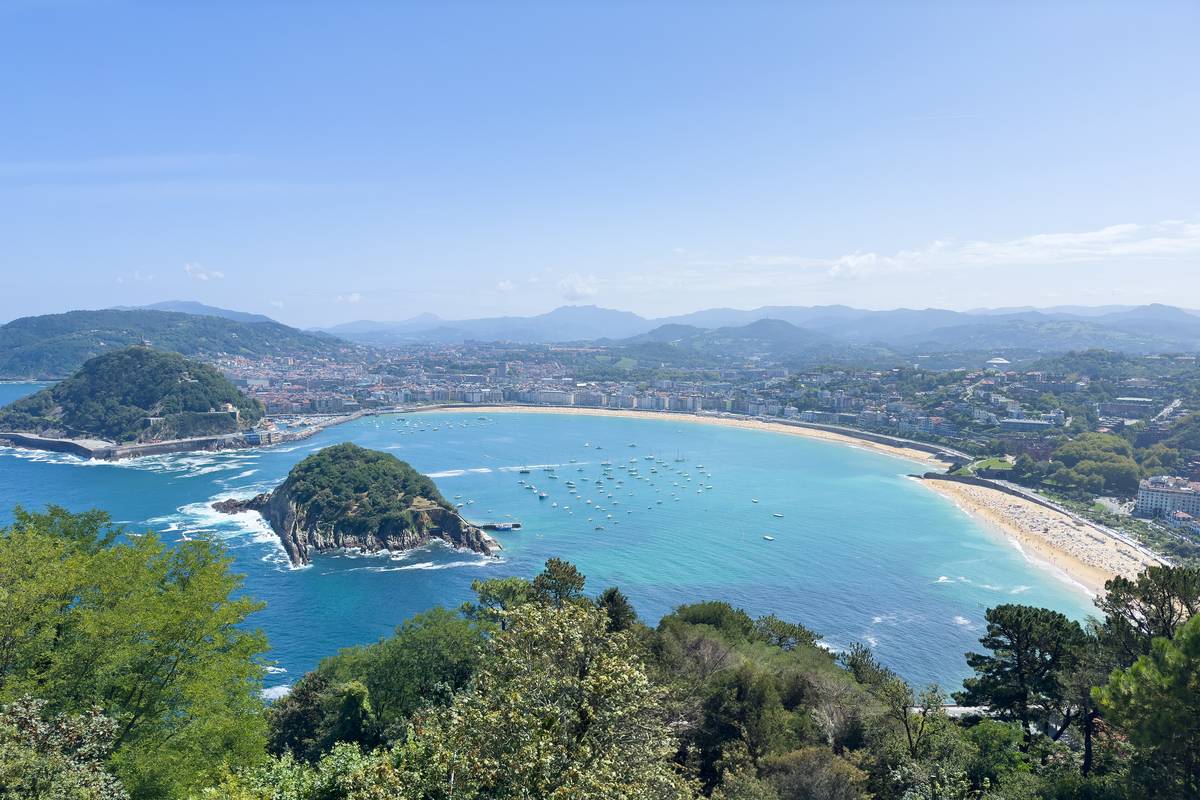 Bukten La Concha i San Sebastián sedd från berget Igueldo, med ön Santa Clara, en lång ljus sandstrand och staden mot gröna berg