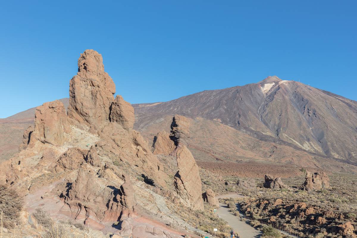 Vulkanen Teide på Teneriffa med ett snöstänk på toppen bakom de rödbruna klippformationerna Roques de García under en klarblå himmel
