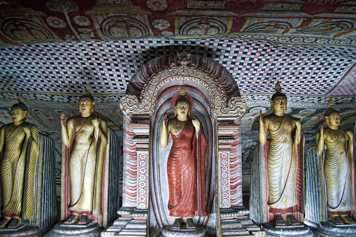 Stående gyllene Buddhastatyer under ett målat klipptak inne i ett av Dambullas grottempel