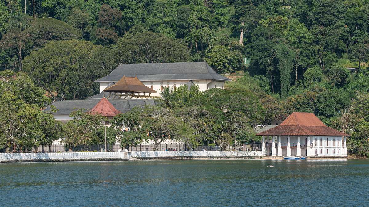 Tandtemplet i Kandy med vita byggnader och rött tak vid stranden av Kandysjön, med gröna träd runt omkring