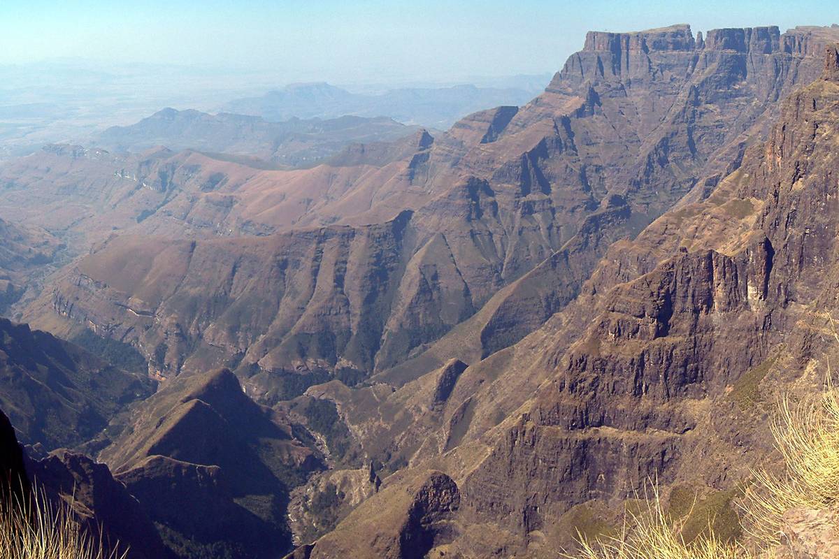 Branta, rödbruna bergväggar och djupa dalar i norra Drakensberg, sedda från kanten av Amfiteatern i varmt ljus
