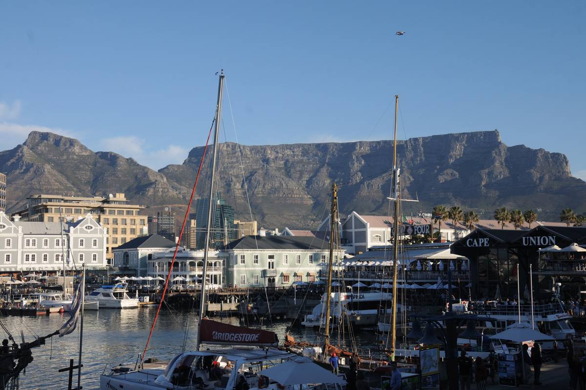 Segelbåtar och vita hus vid hamnen i V&A Waterfront, med Taffelbergets platta topp och Djävulstoppen bakom under en klarblå himmel