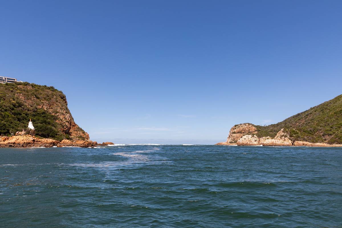 Lagunens mynning mellan de två grönklädda klipporna Knysna Heads, med en liten vit fyr på den vänstra klippan och blått vatten i förgrunden