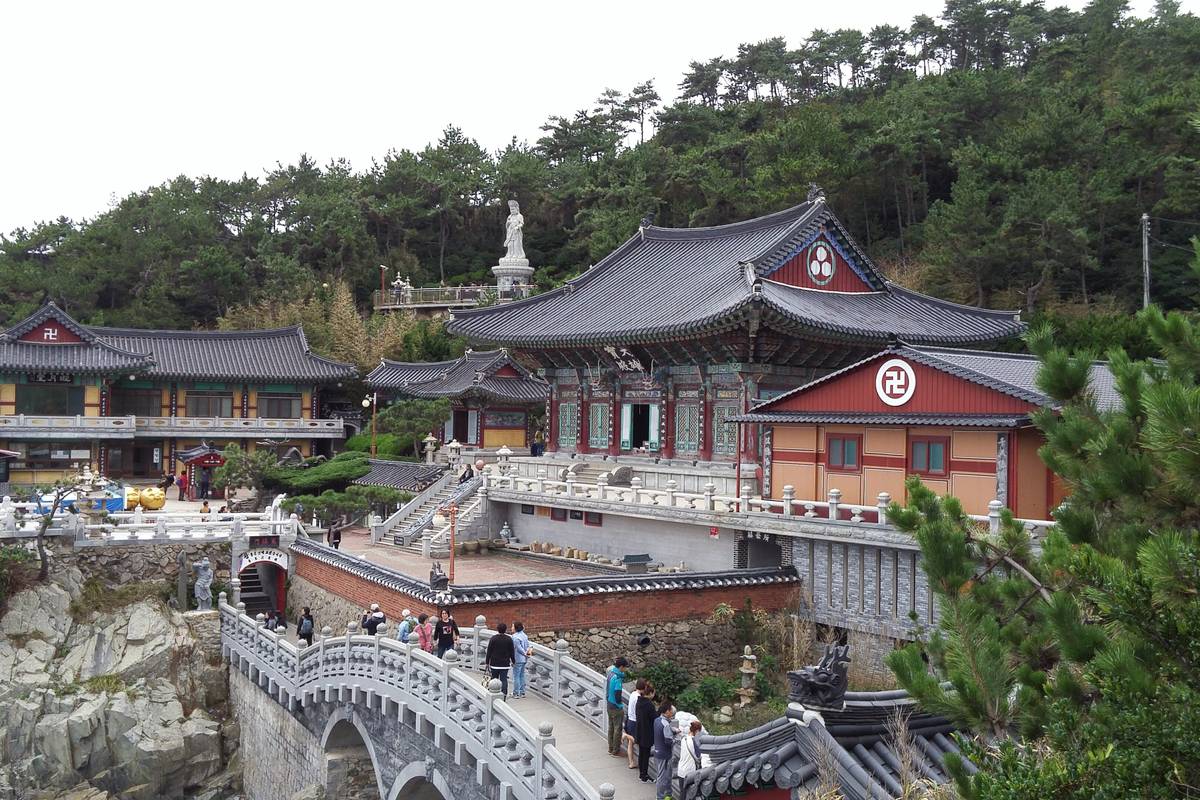 Templet Haedong Yonggungsa med målade träbyggnader och en stenbro på klipporna vid havet utanför Busan, omgivet av tallar