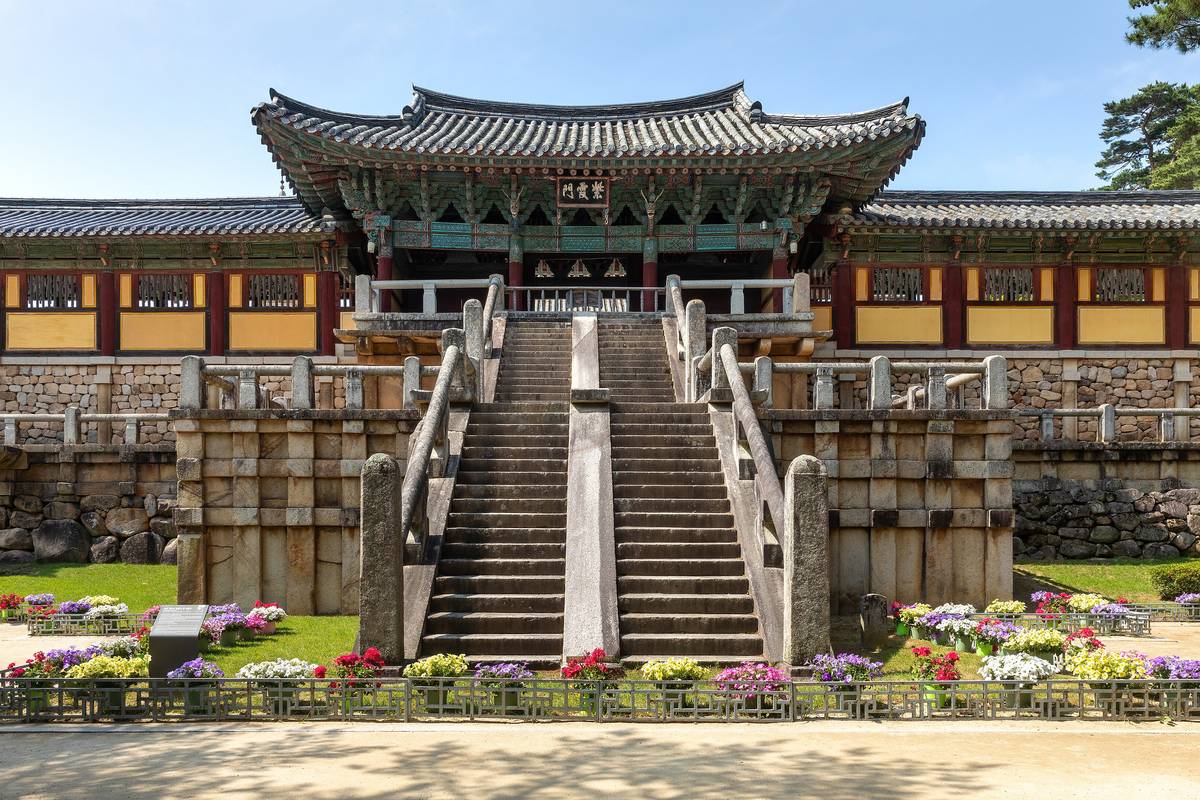 De branta stentrapporna upp till porten vid templet Bulguksa i Gyeongju, med målade träbyggnader, blommor i rabatter och klarblå himmel