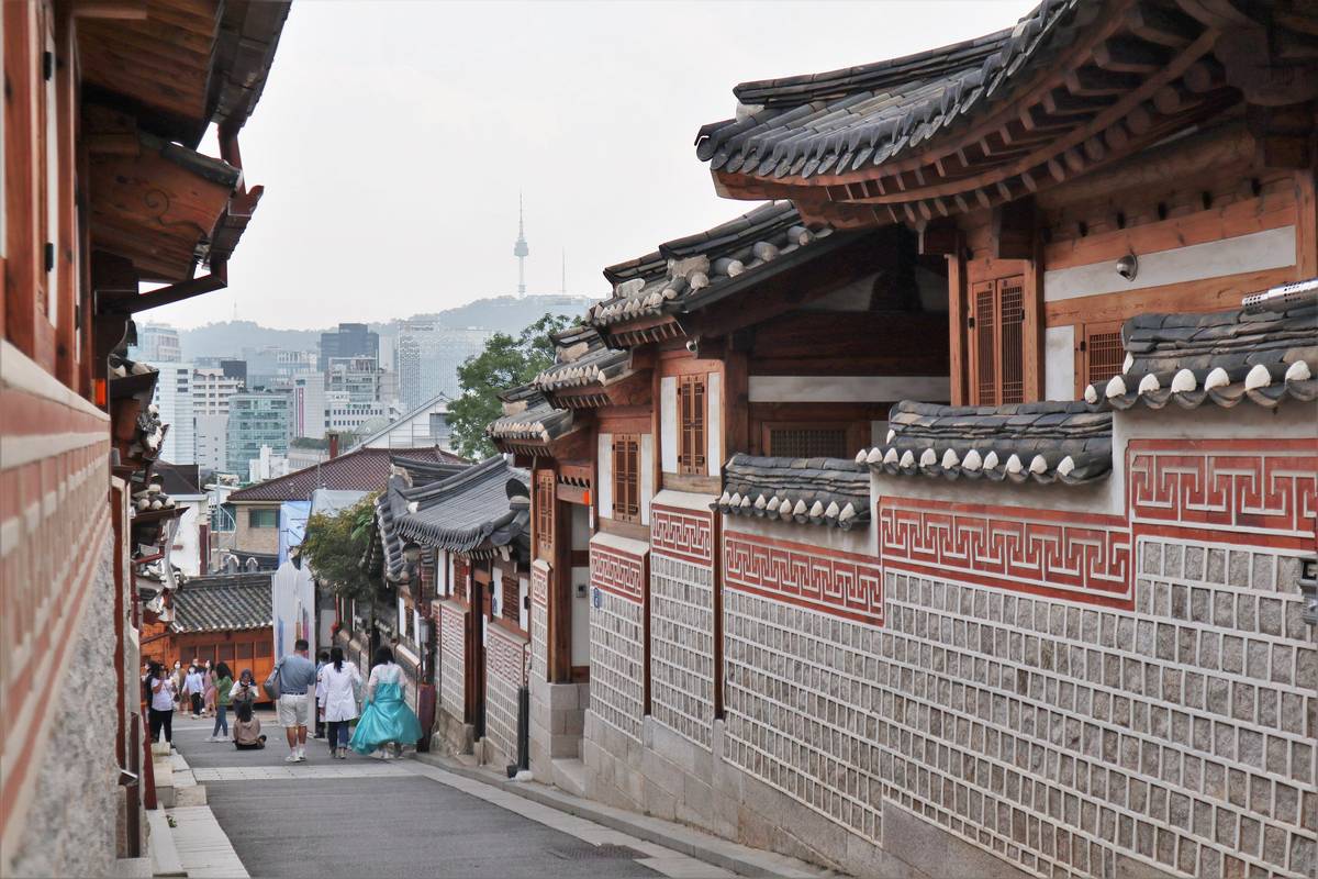 En sluttande gränd i Bukchon med traditionella hanok med böjda tegeltak och mönstrade stenmurar, och tornet N Seoul Tower i fjärran