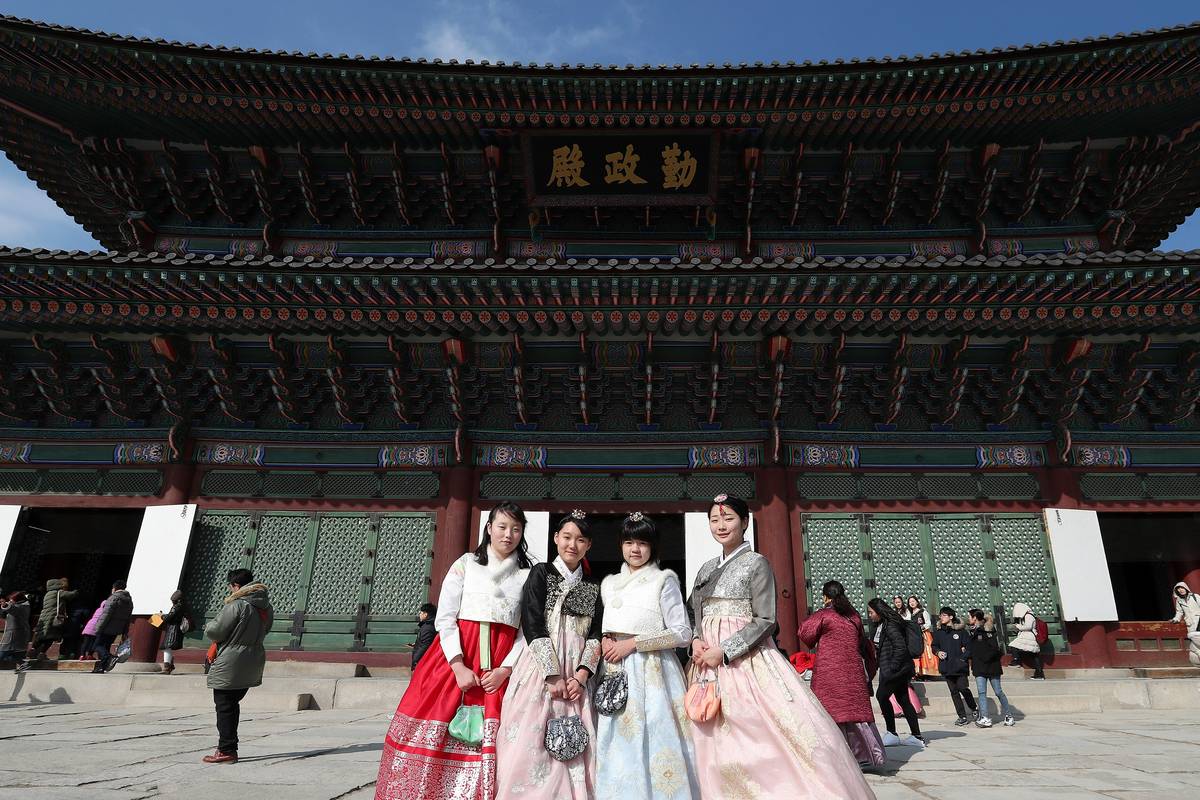 Fyra besökare i färgglada hanbok, de traditionella koreanska dräkterna, framför tronhallen Geunjeongjeon i palatset Gyeongbokgung i Seoul