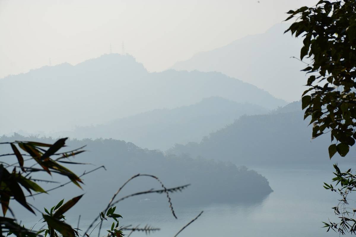 Dimmig morgon över Sun Moon Lake med blåa bergskammar och en grön udde i sjön