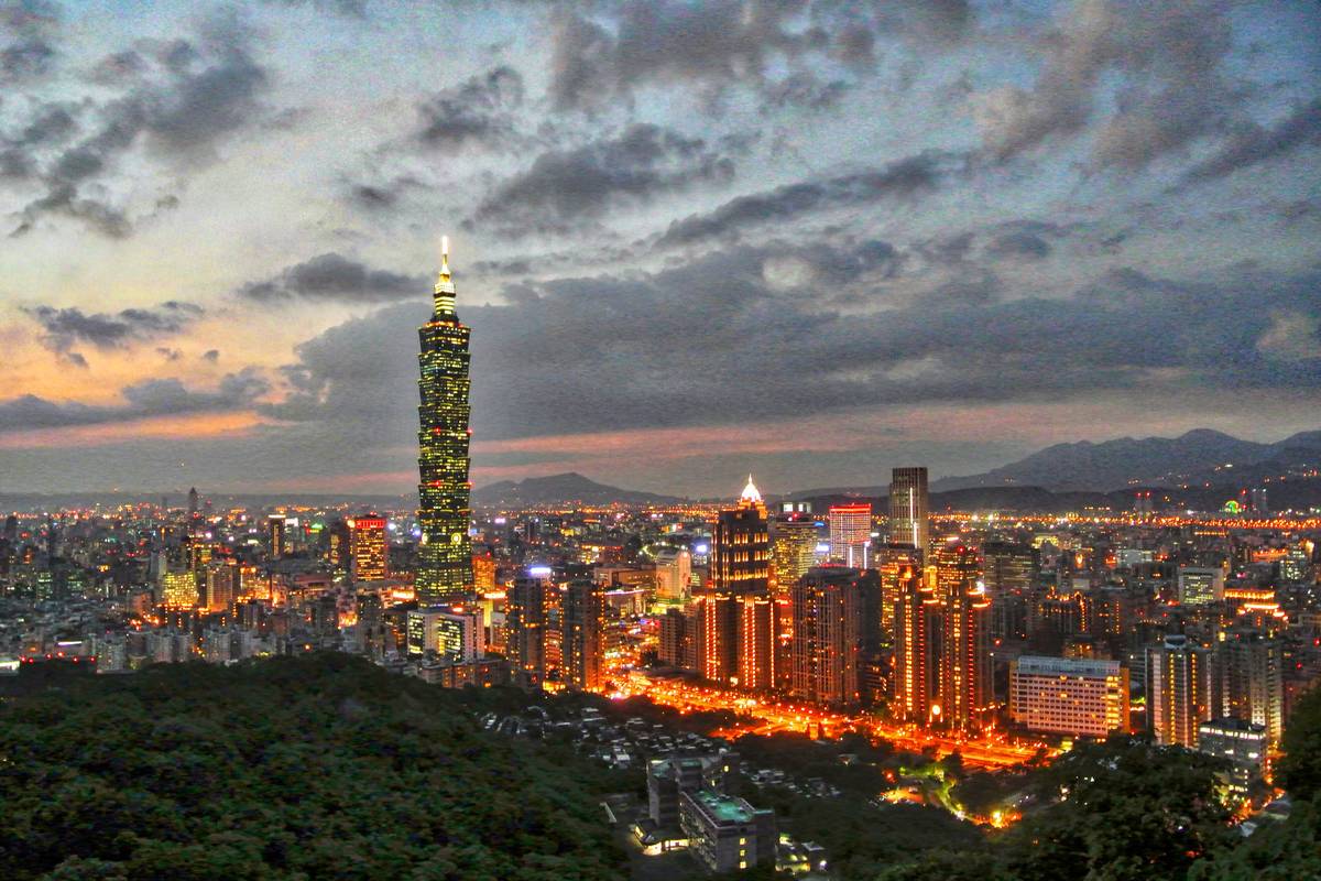 Taipei 101 och stadens ljus i skymningen sedda från Elefantberget, med gröna träd i förgrunden