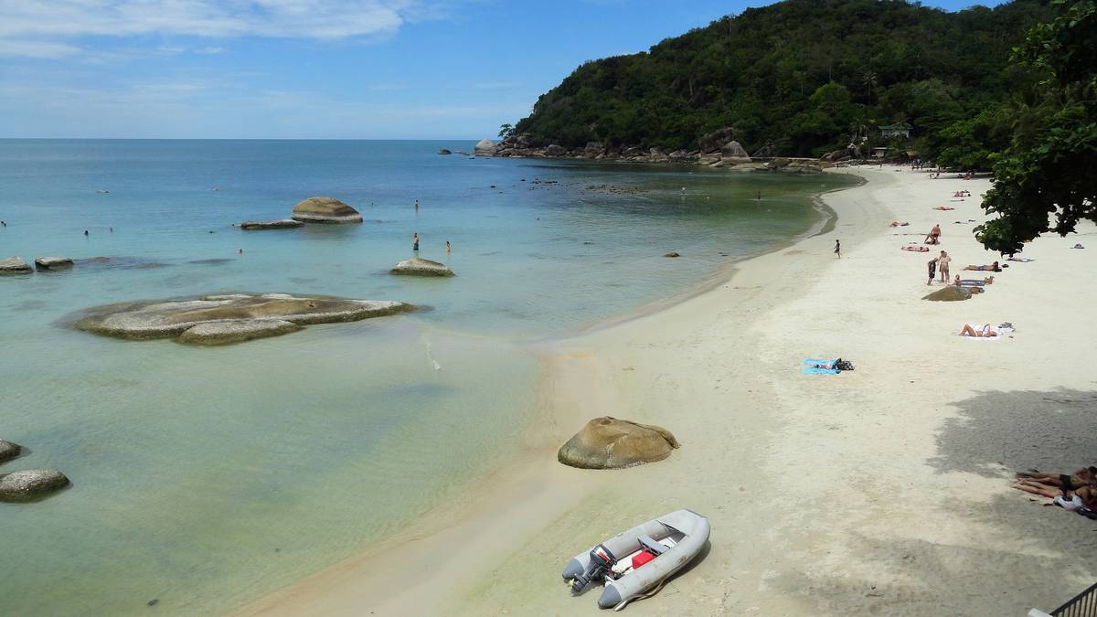 En liten vik med vit sand, klart turkost vatten och runda granitstenar vid Thong Ta Kian på Koh Samui, med en grön udde i bakgrunden