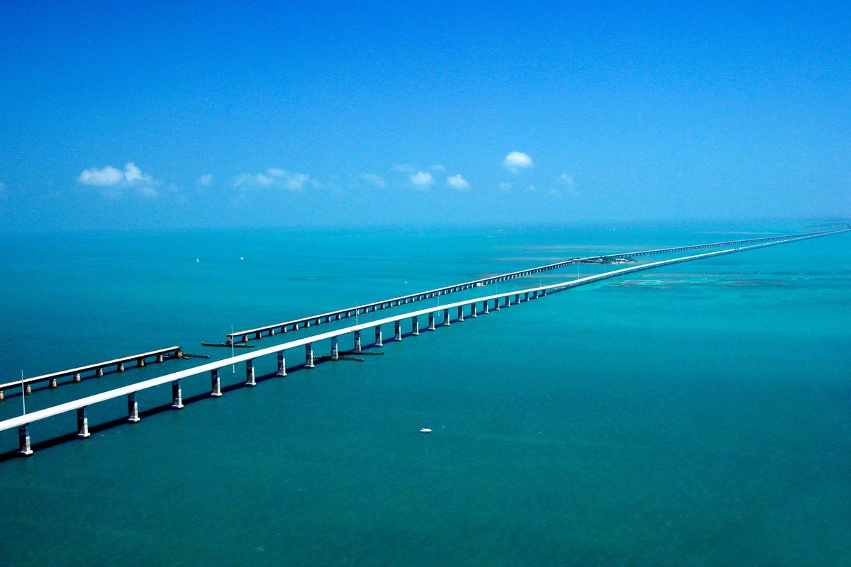 Flygbild över Seven Mile Bridge som sträcker sig rakt ut över det turkosa havet i Florida Keys, med den gamla bron bredvid och små moln vid horisonten