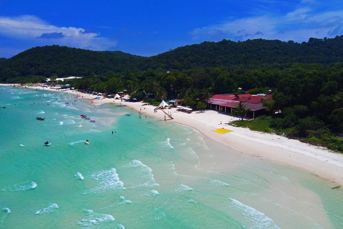 Flygbild över Sao Beach på Phu Quoc, med turkost vatten, vit sandstrand, några strandrestauranger och skogsklädda kullar
