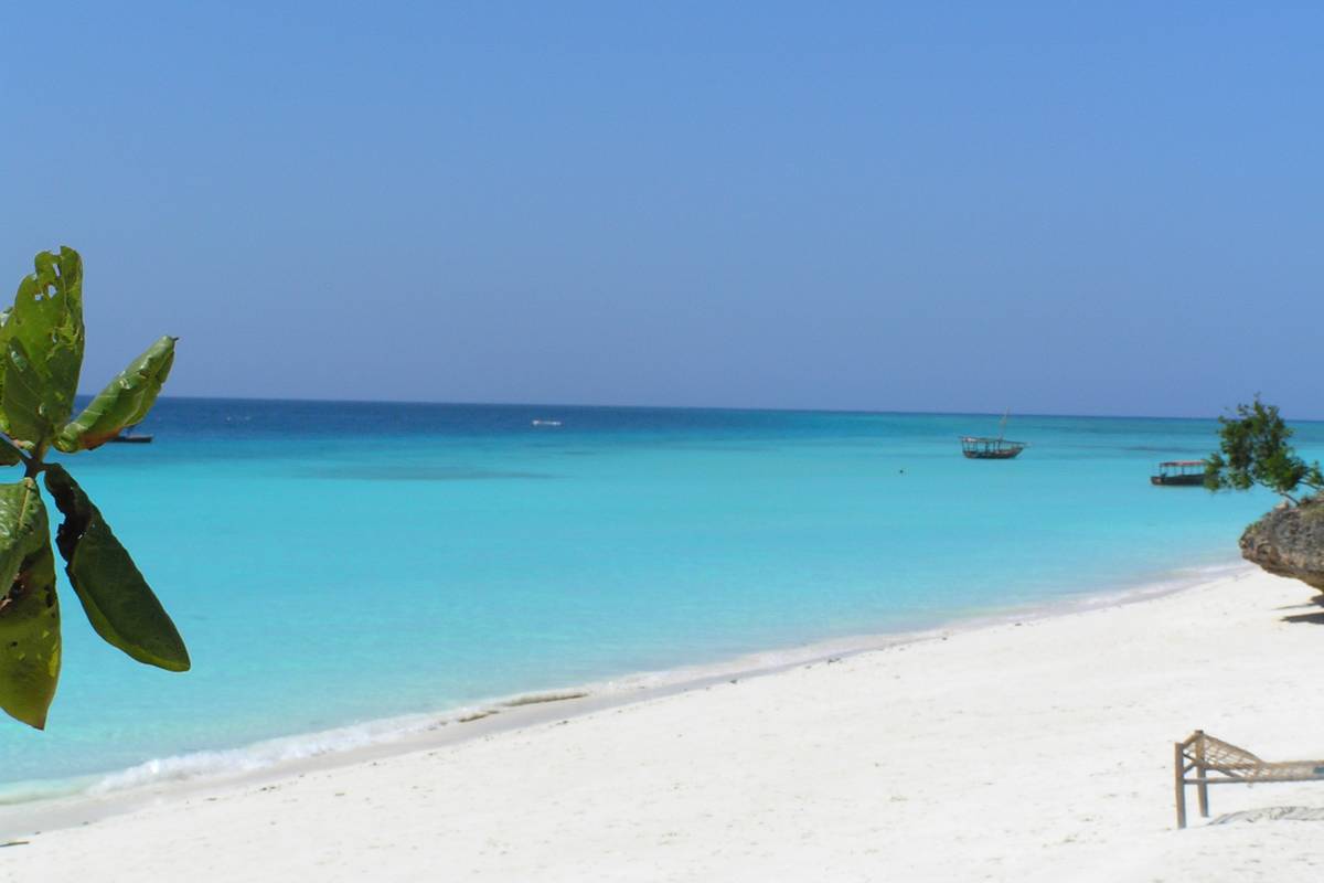 Vit sandstrand vid Nungwi på norra Zanzibar med klart turkost vatten och några båtar längre ut