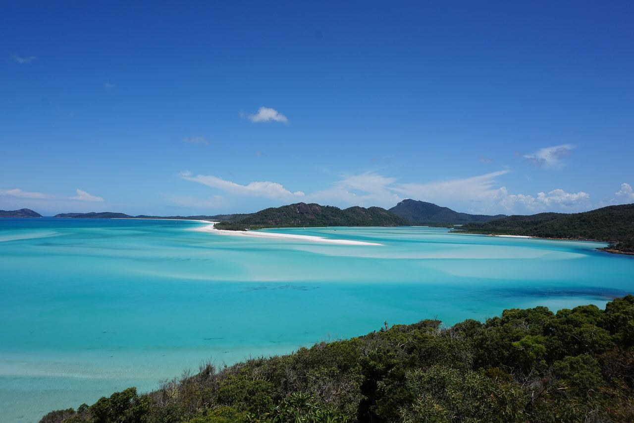 Utsikt över Hill Inlet vid Whitehaven Beach med virvlar av vit sand i turkost vatten, gröna öar och blå himmel