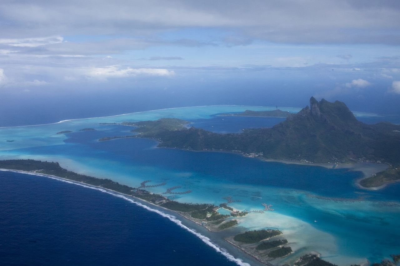 Flygbild över Bora Bora med berget Otemanu, en turkos lagun och det smala korallrevet med palmöar längs ytterkanten
