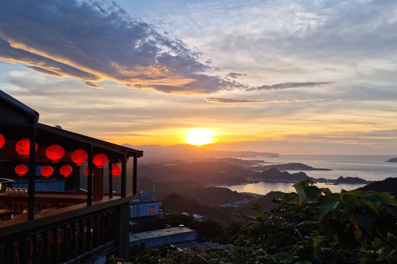 Solnedgång över bergen och havet sedda från Jiufen i Taiwan, med röda lyktor under ett tehustak till vänster